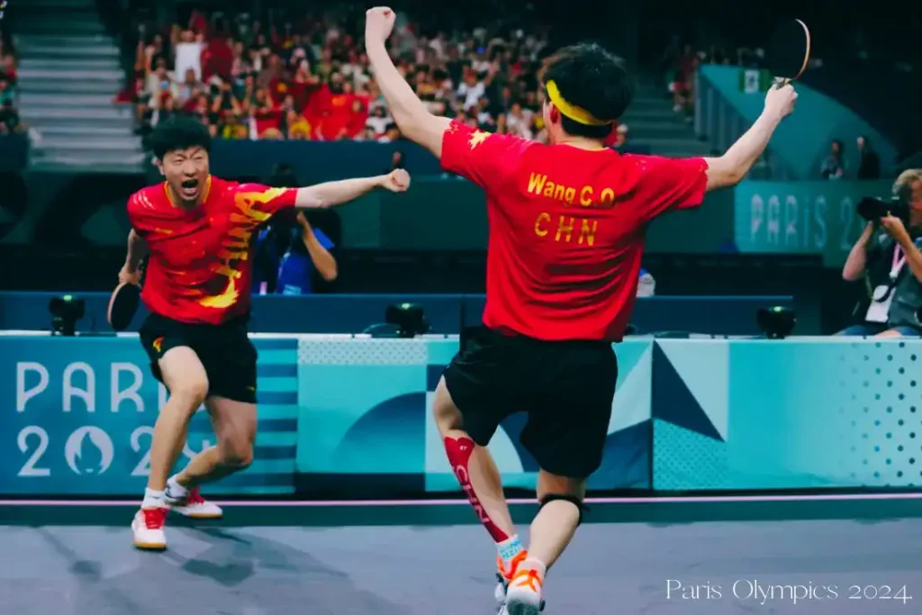 Ma Long and Wang Chuqin celebrate their Paris 2024 Olympic win, beaming with joy and raising their fists.